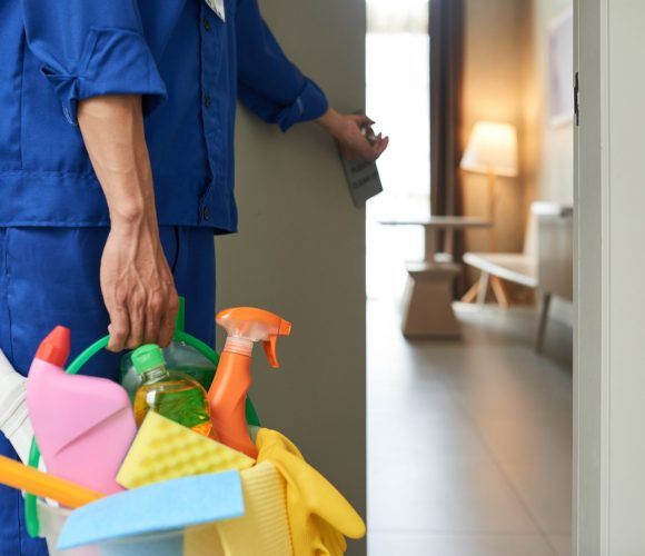 Professional cleaner with bucket of detergents opening room