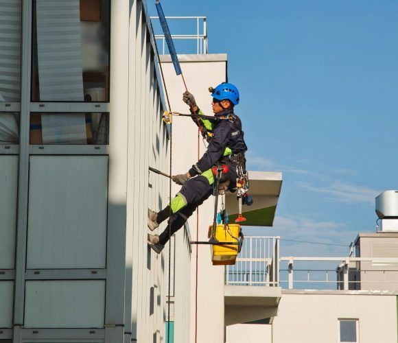 Industrial mountaineering worker hangs over residential facade building while washing exterior facade glazing. Rope access laborer hangs on wall of house. Concept of urban works. Copy space for site